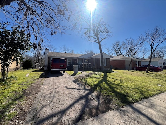 ranch-style house with a front yard, decorative driveway, brick siding, and a chimney