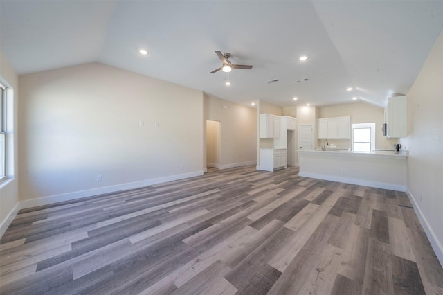 unfurnished living room with a ceiling fan, lofted ceiling, light wood finished floors, and baseboards