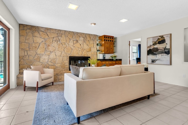 living room with light tile patterned flooring, a stone fireplace, and a textured ceiling