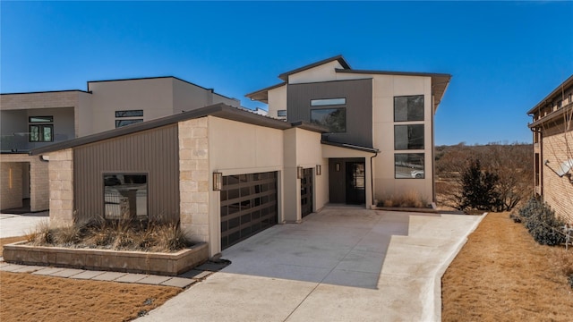 contemporary house with an attached garage, stone siding, concrete driveway, and stucco siding