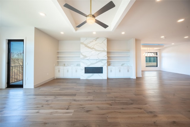 unfurnished living room featuring built in features, a high end fireplace, ceiling fan, and wood finished floors