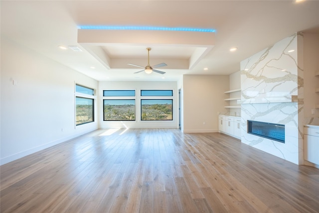 unfurnished living room featuring a tray ceiling, a premium fireplace, built in shelves, and light wood-style floors