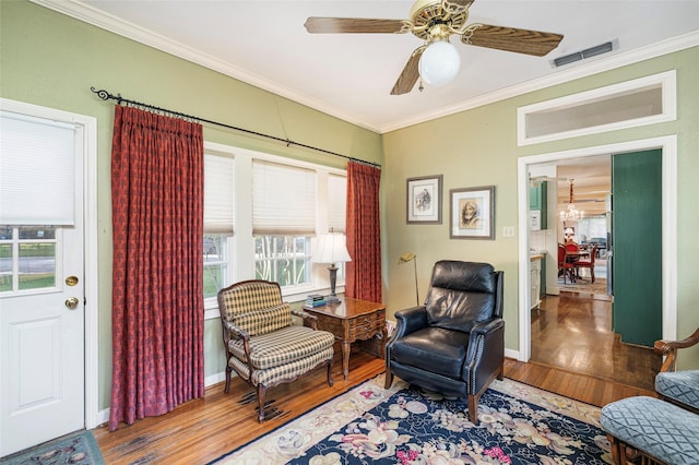 sitting room featuring ceiling fan with notable chandelier, wood finished floors, visible vents, baseboards, and ornamental molding