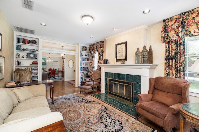 living area with built in shelves, a tile fireplace, visible vents, and wood finished floors