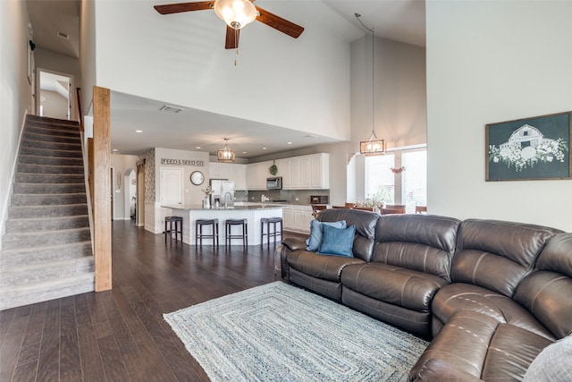 living room featuring ceiling fan, high vaulted ceiling, visible vents, stairs, and dark wood finished floors