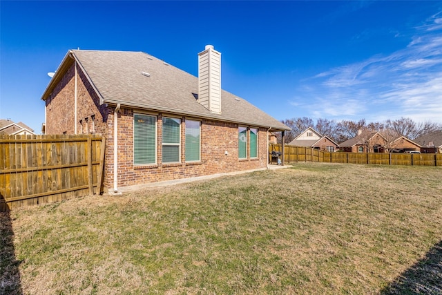 rear view of property with brick siding, a lawn, a chimney, and a fenced backyard