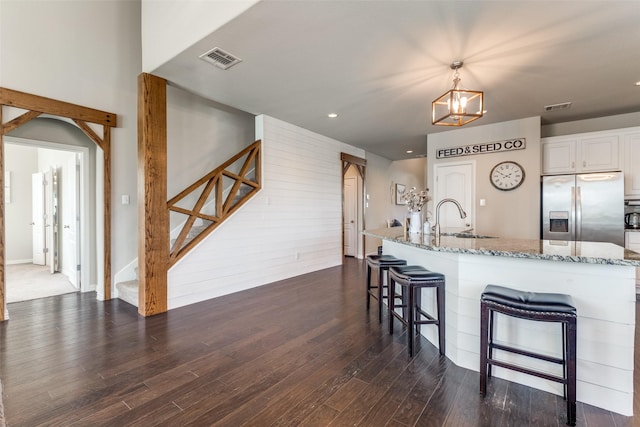 kitchen featuring visible vents, dark wood-style floors, light stone countertops, stainless steel refrigerator with ice dispenser, and a sink