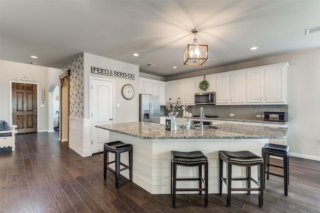 kitchen with arched walkways, white cabinets, dark wood finished floors, stainless steel appliances, and backsplash