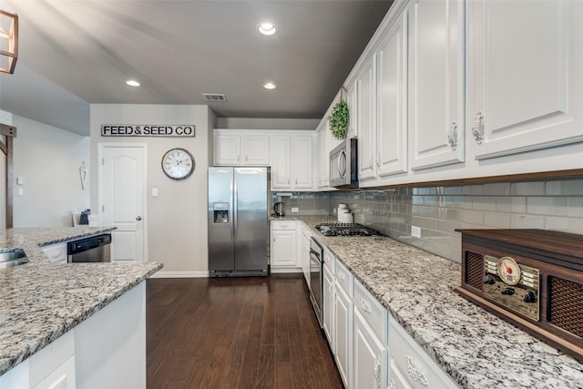 kitchen with tasteful backsplash, dark wood-style floors, light stone countertops, stainless steel appliances, and white cabinetry