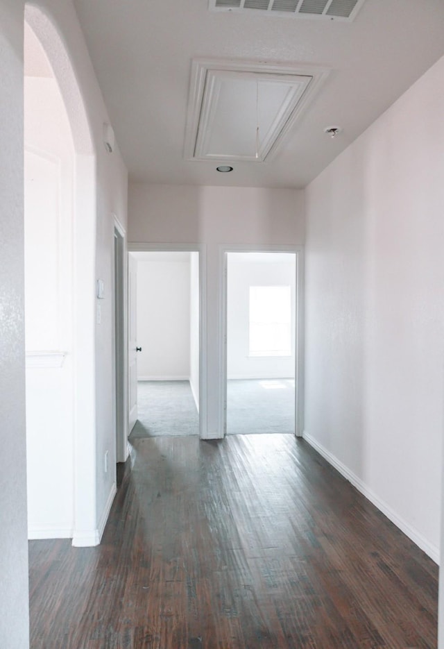 hallway with baseboards, attic access, visible vents, and dark wood-style flooring