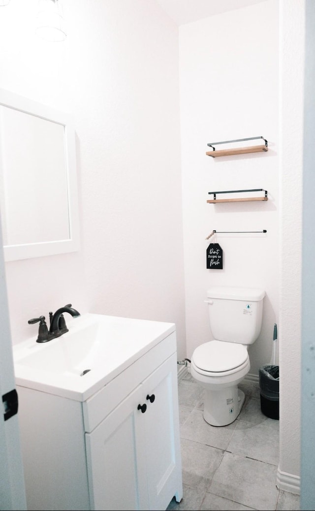 half bath with baseboards, vanity, and toilet