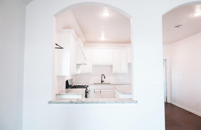 kitchen with stainless steel gas stove, visible vents, white cabinets, light stone countertops, and a sink