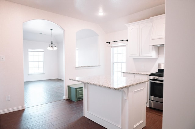 kitchen featuring light stone counters, a center island, dark wood-style flooring, stainless steel range with gas stovetop, and white cabinetry