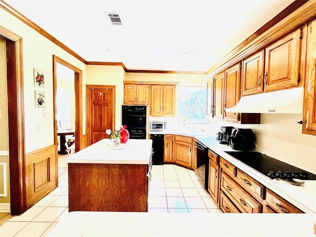 kitchen featuring crown molding, light countertops, wainscoting, under cabinet range hood, and black appliances