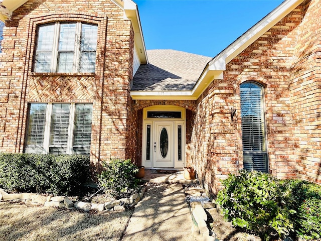 doorway to property with roof with shingles and brick siding