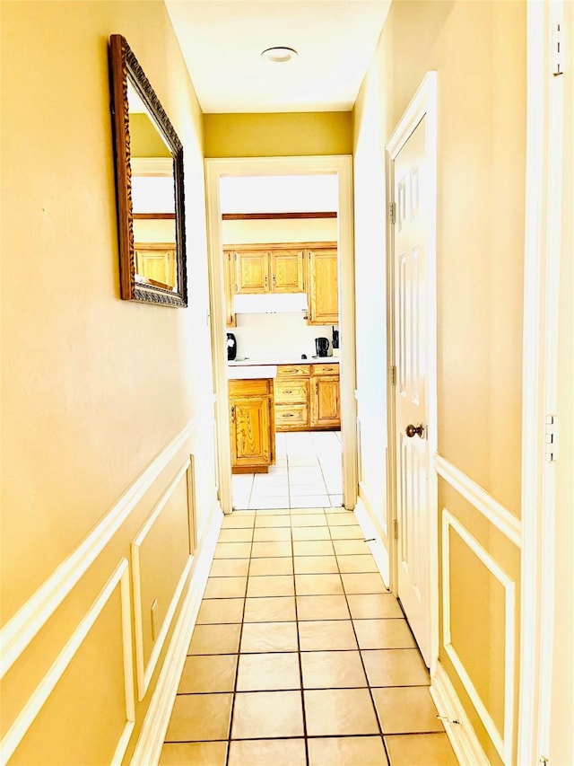 hall with a wainscoted wall, light tile patterned flooring, and a decorative wall