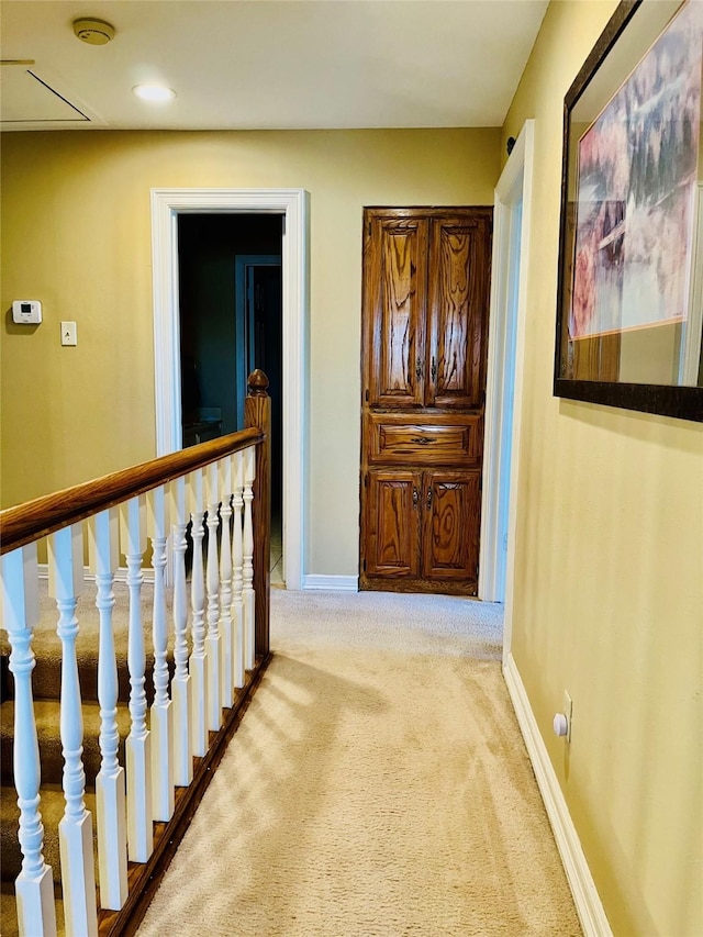 hallway with light carpet, baseboards, and an upstairs landing