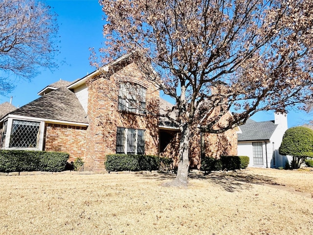 view of front of property featuring brick siding, roof with shingles, and a front yard