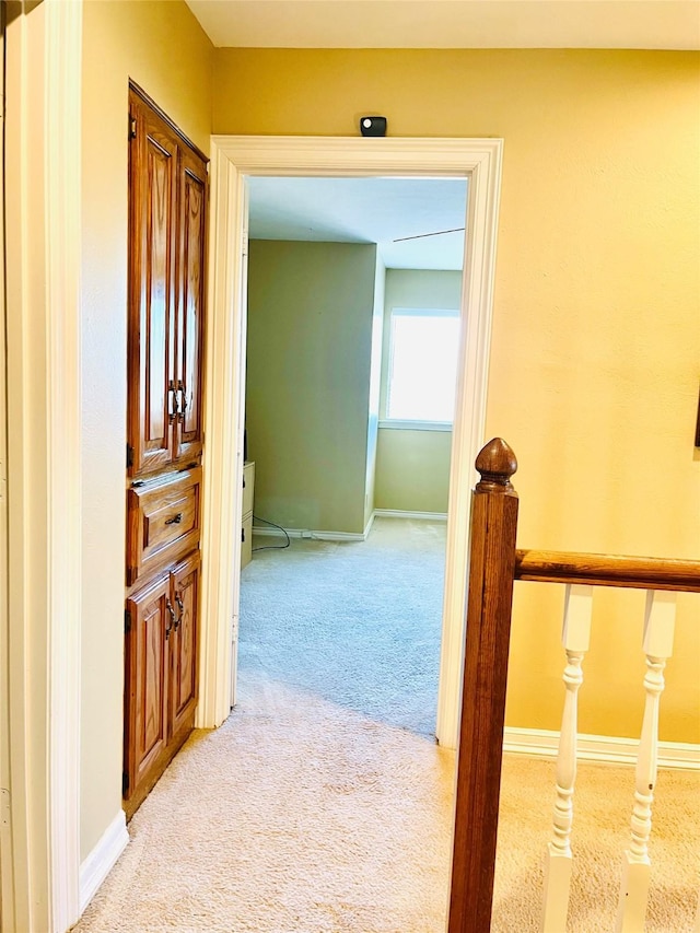 hall with baseboards, an upstairs landing, and light colored carpet