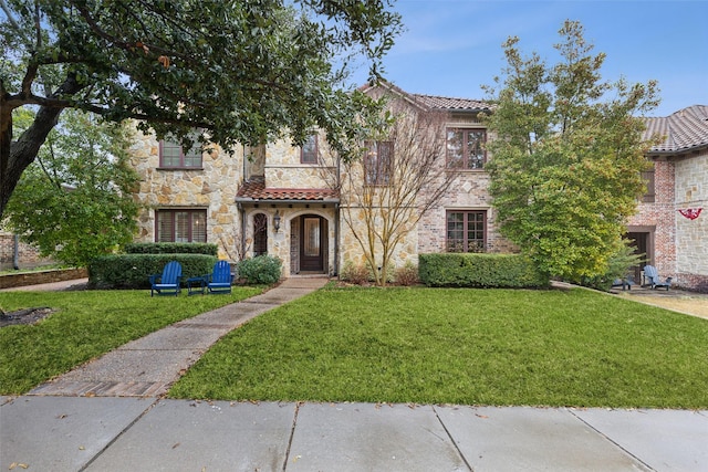 view of front facade with stone siding, a front yard, and a tile roof