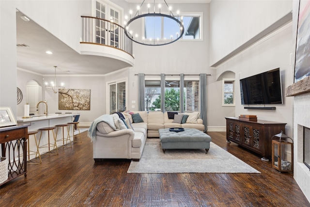 living area with a fireplace, crown molding, dark wood finished floors, a chandelier, and baseboards