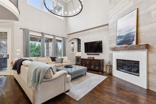 living room featuring arched walkways, a notable chandelier, a tiled fireplace, and wood finished floors