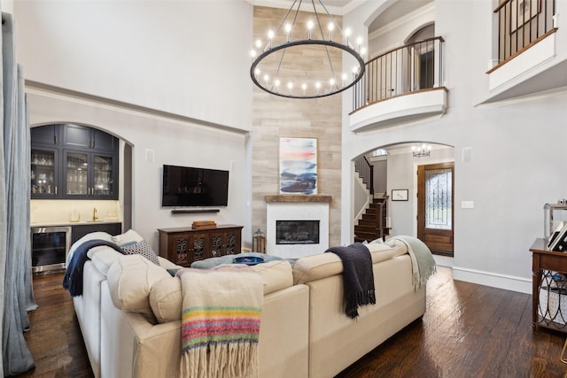 living area with indoor bar, a towering ceiling, dark wood-style floors, wine cooler, and an inviting chandelier