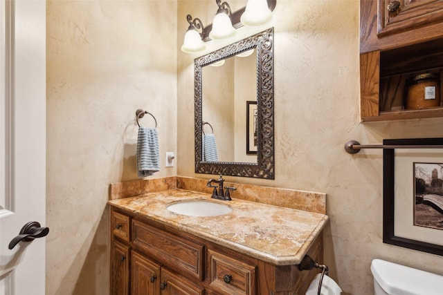 half bathroom featuring toilet, a textured wall, and vanity