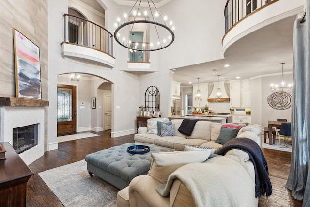 living area with dark wood-style flooring, crown molding, a notable chandelier, a large fireplace, and baseboards