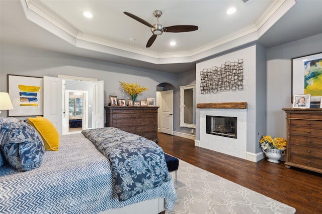 bedroom with a tray ceiling, a glass covered fireplace, arched walkways, and wood finished floors