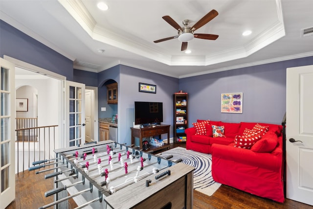 recreation room with ornamental molding, arched walkways, a raised ceiling, and wood finished floors