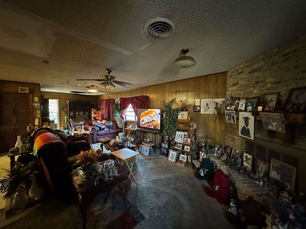 living room featuring carpet floors, visible vents, a ceiling fan, a textured ceiling, and wooden walls