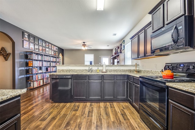 kitchen with arched walkways, a peninsula, dark wood-style flooring, a sink, and black appliances