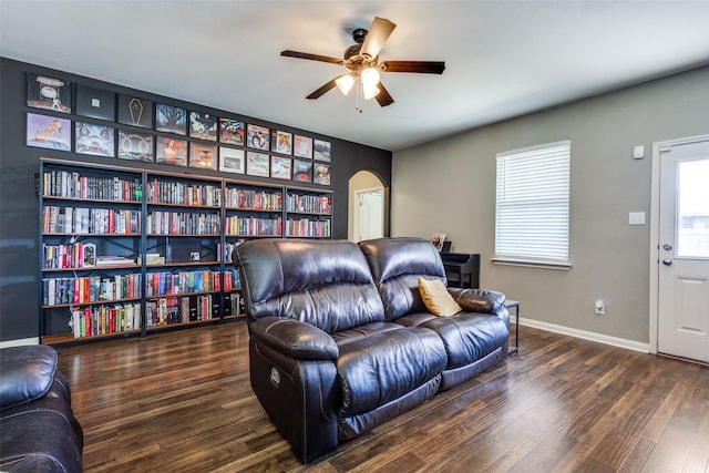 living area with arched walkways, wood finished floors, a ceiling fan, and baseboards