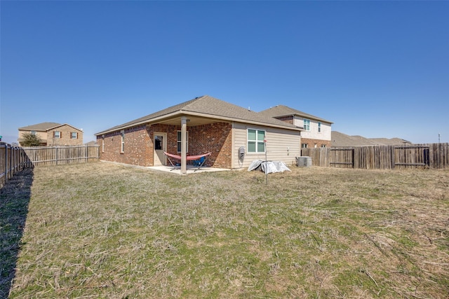 rear view of property featuring brick siding, a patio, central air condition unit, a lawn, and a fenced backyard