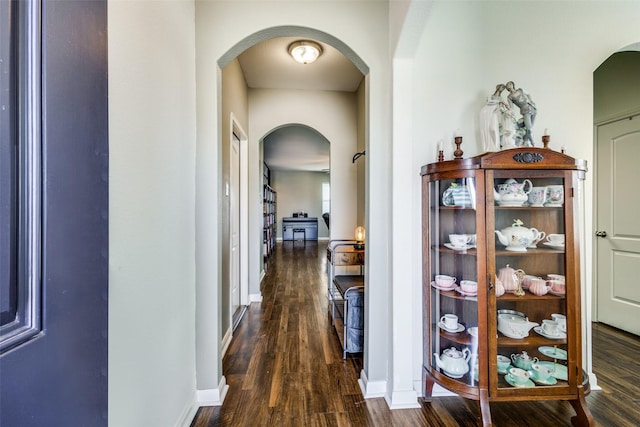 hall with dark wood-style floors, arched walkways, and baseboards