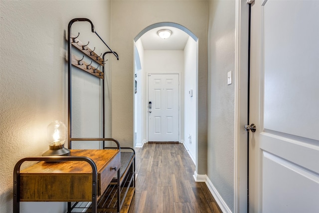 doorway featuring a textured wall, arched walkways, dark wood finished floors, and baseboards