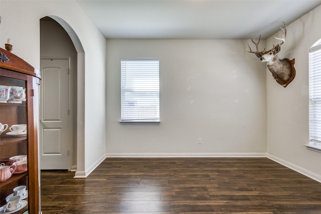 interior space featuring arched walkways, dark wood finished floors, and baseboards