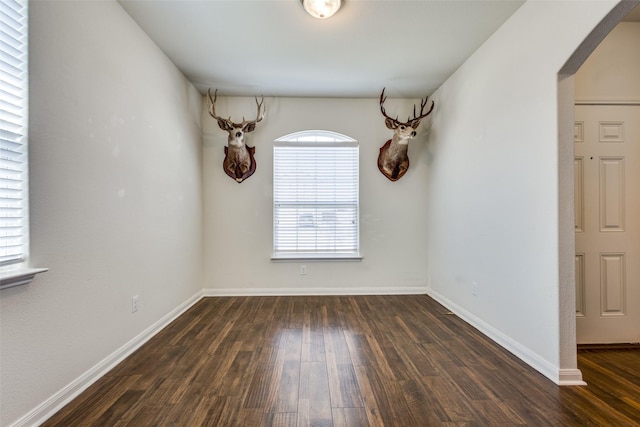 unfurnished dining area with baseboards, arched walkways, and wood finished floors