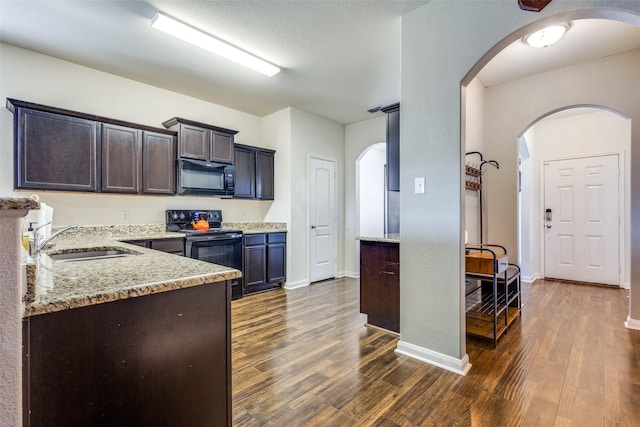 kitchen featuring dark wood-type flooring, a sink, dark brown cabinets, light stone countertops, and black appliances