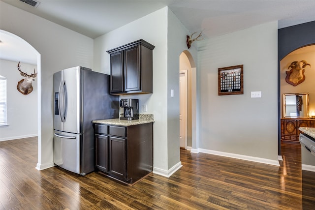 kitchen featuring arched walkways, dark wood finished floors, light stone countertops, stainless steel fridge, and dishwasher