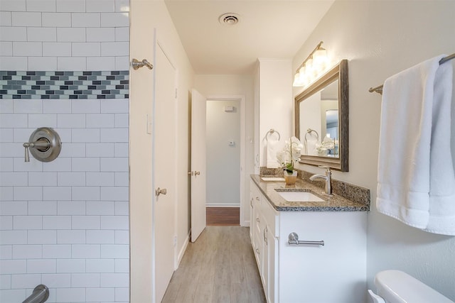 bathroom featuring visible vents, a shower, toilet, wood finished floors, and vanity