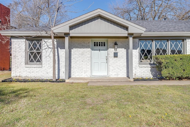 doorway to property with brick siding, roof with shingles, and a yard