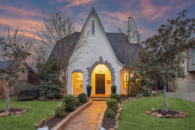 view of front of home with a shingled roof, a lawn, and brick siding