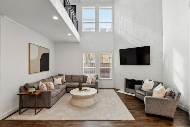 living area featuring dark wood-style flooring, a fireplace, a towering ceiling, ornamental molding, and baseboards