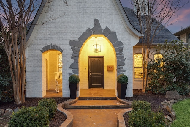 view of exterior entry featuring a shingled roof and brick siding