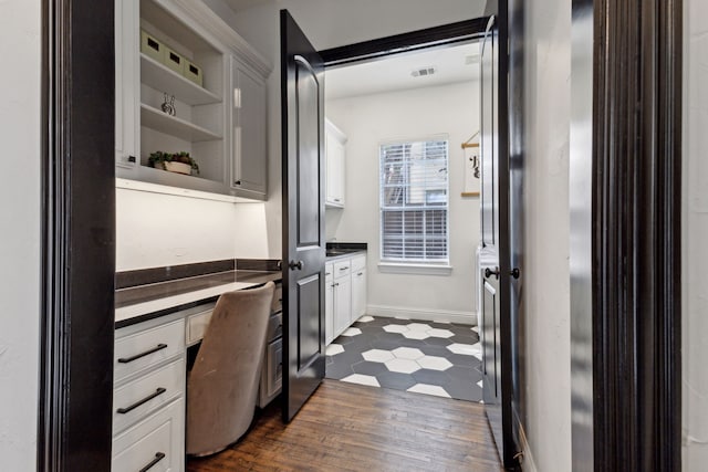 office space featuring baseboards, visible vents, dark wood finished floors, and built in desk