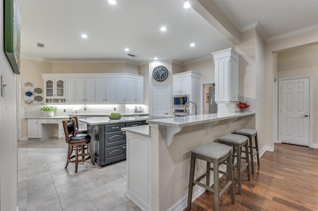 kitchen featuring a peninsula, a breakfast bar, white cabinetry, backsplash, and stainless steel microwave