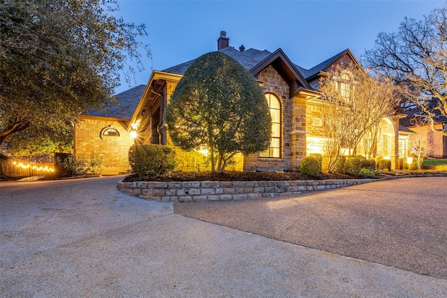 view of front of home with stone siding, brick siding, driveway, and a chimney