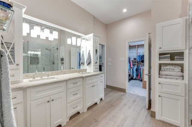 full bathroom with double vanity, wood finished floors, a sink, and a shower stall